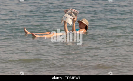 Mar Morto, Israele - SETTEMBRE, 22, 2016: donna leggendo un giornale mentre galleggianti in Israele il mar morto Foto Stock