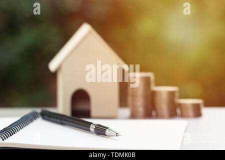 Aziendali e finanziarie il concetto di proprietà per la casa prestito, ipoteca, di risparmio e di investimento. La penna nera sul notebook in bianco con stack sfocata di monete e una Foto Stock