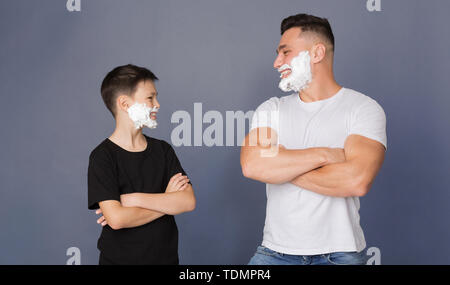 Papà e figlio con schiuma da barba sulle facce in piedi con le mani incrociate Foto Stock