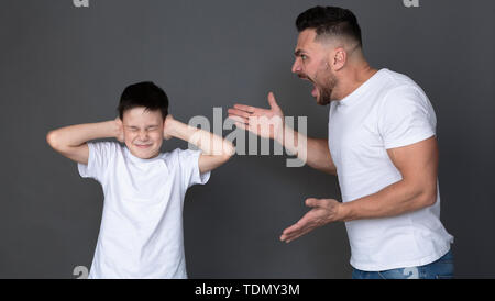 Furious papà urlando al suo figlio, spaventata bambino chiudere gli occhi e le orecchie Foto Stock