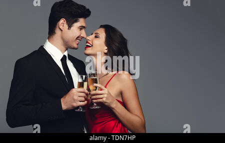 Felice coppia giovane avente lo champagne contro uno sfondo grigio. Bel giovane e bella donna in abito elegante con champagne e sorridente. Foto Stock