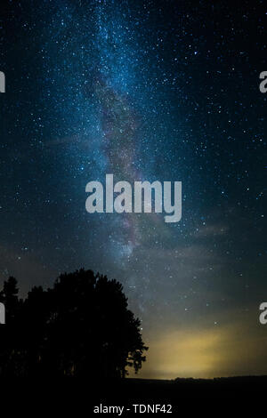 Paesaggio notturno con colorati Via Lattea e una luce gialla a montagne. Cielo stellato con le colline in estate. Bella universo. Sfondo spazio Foto Stock