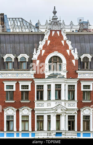 La facciata di un vecchio edificio in mattoni rossi con stucco bianco di finestre e balconi nella parte vecchia di Riga. Foto Stock