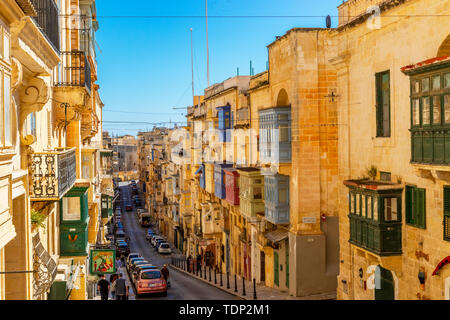 Tipica maltese strette strade con i tradizionali colorati finestre e persiane di legno e balconi, cielo blu chiaro su un giorno di estate, Valletta, Malta Foto Stock