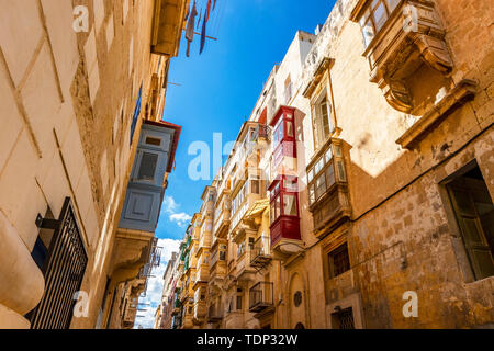 Tipica maltese strette strade con i tradizionali colorati finestre e persiane di legno e balconi, cielo blu chiaro su un giorno di estate, Valletta, Malta Foto Stock