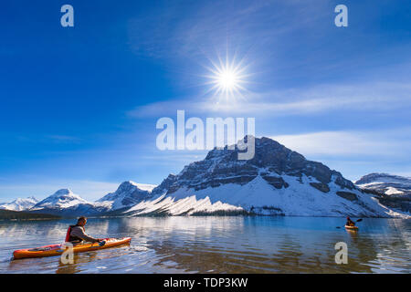 Fotografato a Bow Lake, il Parco Nazionale di Banff, Canada, appassionati di nautica sono visibili sulla riva come si preparano per ottenere pronto per andare in acqua. Ho preso un'inquadratura dal basso sulla riva, in modo che il caposquadra, mid-vista montagne neve e il lungo raggio di energia solare sono state integrate in una foto allo stesso tempo. E la barca appassionato di arco è stato a destra in direzione del sole, il significato di muoversi verso la luce. Foto Stock