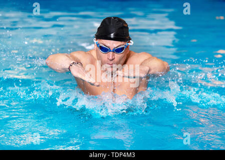 Nuotatore muscolare giovane nel cappuccio nero in piscina, esecuzione di corsa a farfalla . Foto Stock