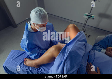 Chirurgo di esaminare la donna incinta durante la consegna in sala operatoria Foto Stock