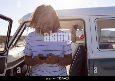 Giovane uomo utilizzando il telefono cellulare vicino a van a beach Foto Stock