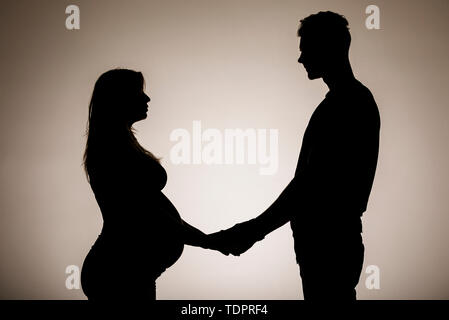 Una silhouette in uno studio di un giovane che stanno avendo un bambino e tenendo le mani mentre la madre è ben lungo nel suo stato di gravidanza Foto Stock