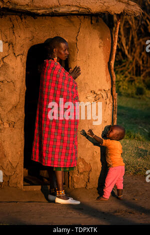 Donna in shuka con bambino capanna esterna; Tanzania Foto Stock