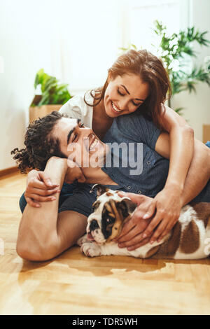 La giovane coppia felice si trasferisce in una nuova casa. Sono sdraiato sul pavimento con il loro piccolo cucciolo dopo che avevano portato a caselle con cose da th Foto Stock