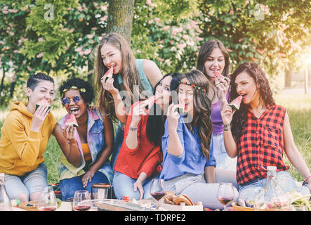 Le fanciulle felici mangiando anguria a cena al sacco in giardino - Giovani donne divertirsi godendosi il pranzo insieme nel cortile posteriore Foto Stock