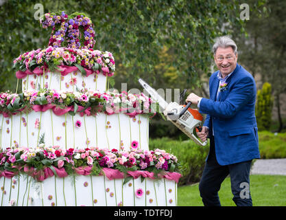 TV giardiniere Alan Titchmarsh finge di tagliare tre giganti-tiered floreali torta di compleanno con una motosega per contrassegnare 70 anni di RHS Garden Harlow Carr, durante la RHS Garden Harlow Carr Flower Show in Harrogate, North Yorkshire. Foto Stock