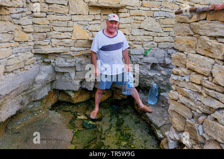 L'uomo ottenendo la sua acqua minerale dal pozzetto, Moldavia, Delacau Foto Stock