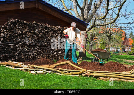 Uomo che lavora in un giardino, la pila di legno, monte di abbaio di pacciame e Barrow, in Germania, in Renania settentrionale-Vestfalia Foto Stock