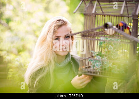 Giovane donna bionda con la birdcage in un giardino, Germania Foto Stock