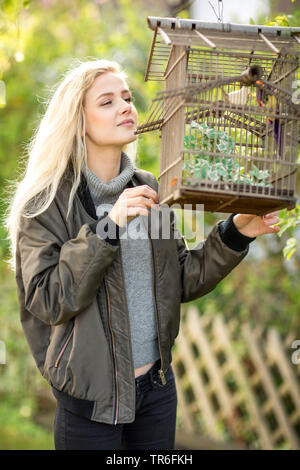 Giovane donna bionda guardando al di fuori di un cagebird in una birdcage, Germania Foto Stock