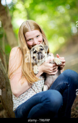Cane domestico (Canis lupus f. familiaris), accovacciato giovane donna tenendo un carino Puggle sul giro, Germania Foto Stock