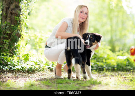 Pastore australiano (Canis lupus f. familiaris), cucciolo con una giovane donna su un sentiero di bosco, Germania Foto Stock