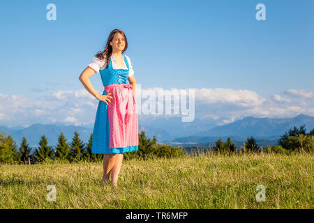 Giovane donna in grembiule in piedi su un prato di montagna, in Germania, in Baviera Foto Stock