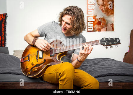 Giovane uomo a suonare la chitarra sul letto, Germania Foto Stock