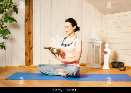 La donna a praticare yoga su un materassino yoga nel piatto con Singing Bowl, Germania Foto Stock