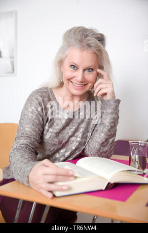Senior femminile seduto alla scrivania e la lettura di un libro, Germania Foto Stock