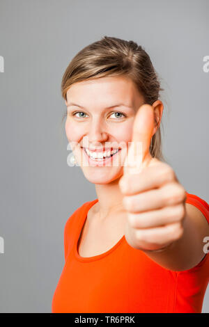 Giovane donna felice, che frolicsome mostrando pollice in alto, Germania Foto Stock