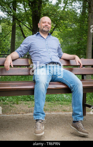 Uomo con la barba e la testa calva seduta su una panchina in natura, Germania Foto Stock