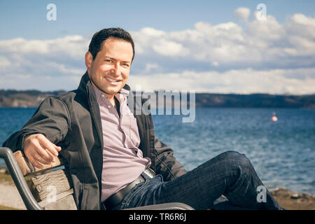 Uomo seduto su una panchina in un lago, Germania Foto Stock