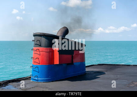Il fumo proveniente da ferry boat canna fumaria durante il mare con la luce solare, acqua di mare e cielo blu in background, Thailandia. A bordo del camino di un traghetto o una nave da crociera, fumi Foto Stock