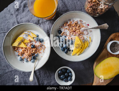 Vista superiore del tavolo per la colazione per due persone, crunchy granola con frutti di bosco freschi e crema di latte o latte. Appartamento laico, mangiare sano. Foto Stock