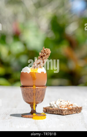 Uova sode in eggcup con fetta di pane tostato bianco sul tavolo di legno in natura sfondo, close up Foto Stock