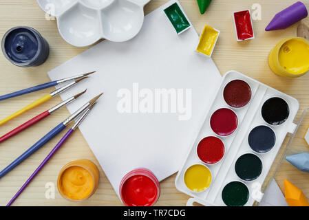 Concetto di arte: composizione con piccoli vuoti di tela bianca, circondata da spazzole, vernici e la tavolozza dei colori su un sfondo di legno, con spazio per il testo Foto Stock