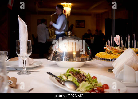 Servita la cena table.piatto caldo sulla cupola il vassoio sulla tavola del server su uno sfondo sfocato giocando il sassofonista per gli ospiti. Foto Stock