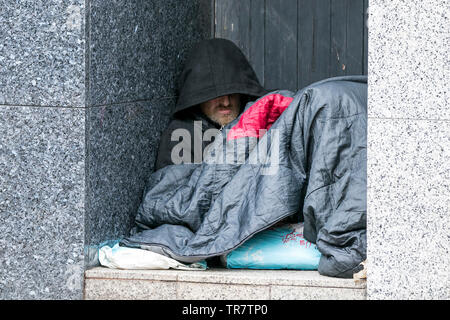 Un senzatetto uomo dorme in un portale di freddo umido strada di città in Preston, Lancashire, Regno Unito Foto Stock