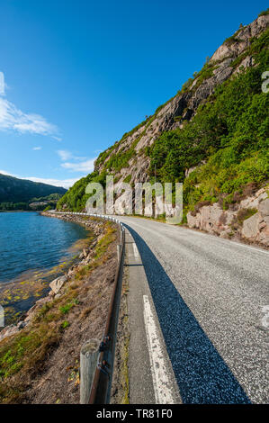 Strette e tortuose strada mediante un fiordo e ripide scogliere sopra. Foto Stock