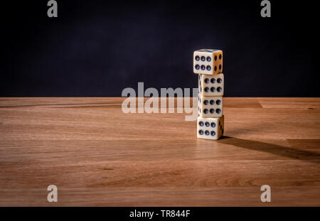 Una pila di dadi su un tavolo di legno contro uno sfondo nero. Foto Stock