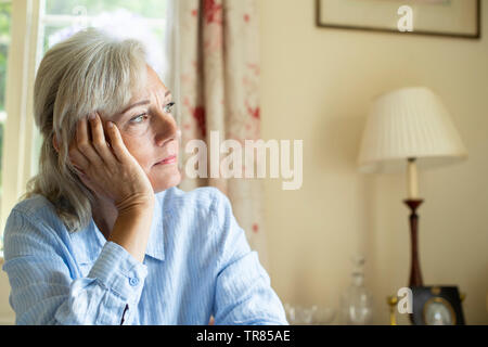 Senior donna soffre di depressione guardando fuori della finestra a casa Foto Stock