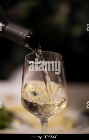 Il vino bianco che viene versato nel bicchiere di vino dalla bottiglia Foto Stock