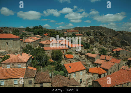 Tetti di pietra antiche case con le cime degli alberi frondosi e grande parete a Sortelha. Un sorprendente e ben conservato borgo medievale in Portogallo. Foto Stock