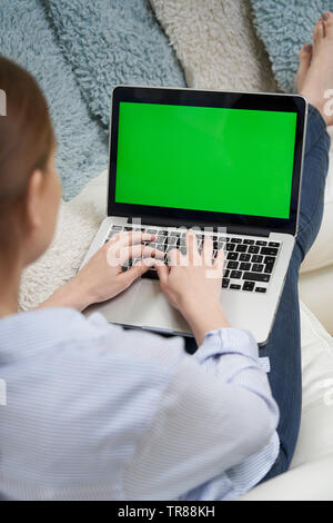 Al di sopra della spalla della donna sdraiata sul divano con schermo verde Laptop Foto Stock
