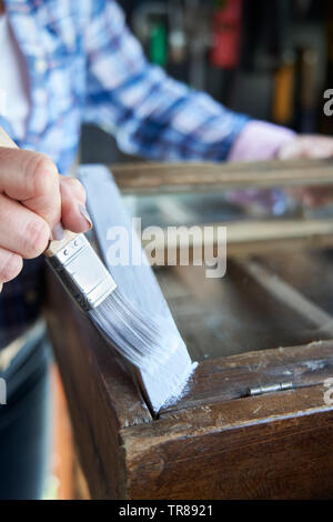 Close Up di donna matura Upcycling mobili in officina a casa armadio dipinto Foto Stock