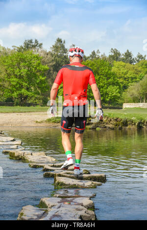 OGMORE DAL MARE, GALLES - Aprile 2019: Persona in abbigliamento ciclo attraversando le pietre miliari attraverso il Fiume Ogwr in Ogmore dal mare nel Galles del Sud Foto Stock