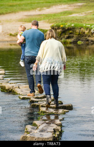 OGMORE DAL MARE, GALLES - Aprile 2019: due persone a piedi attraverso le pietre miliari attraverso il Fiume Ogwr in Ogmore dal mare nel Galles del Sud. Foto Stock