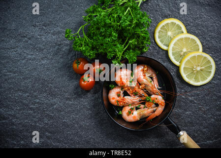 Piatto di frutti di mare con gamberi cotti in padella con erbe e spezie pomodoro limone e prezzemolo riccio su sfondo scuro Foto Stock