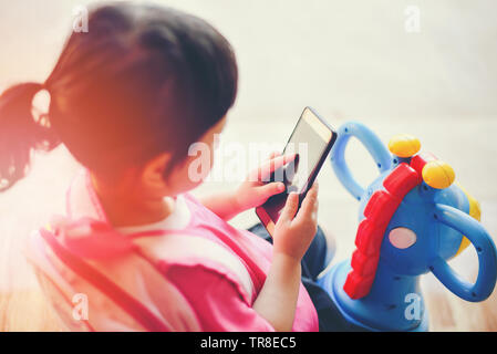 Ragazza tenere il telefono in mano e la riproduzione di smartphone guardando cartoni animati a scuola / Asia bambino 2-3 anni di capretti addicted ai giochi problemi di childr Foto Stock