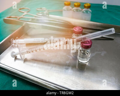 Attrezzature strumenti medicali / siringa ago di iniezione di farmaco medicale nel vassoio in acciaio per infermiere o medico chirurgico verde sulla tabella di tessuto Foto Stock