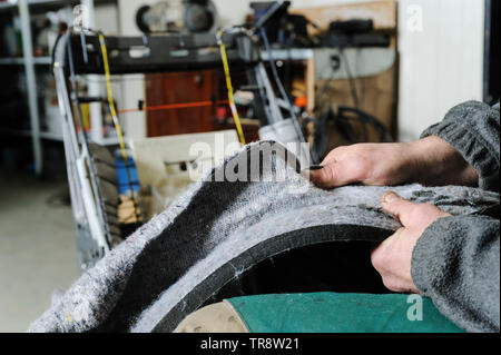 Riparazione del riscaldamento del sedile dell'auto. Le mani del meccanico dell'automobile stanno smontando la tappezzeria di una sedia per raggiungere un cavo di riscaldamento. Foto Stock